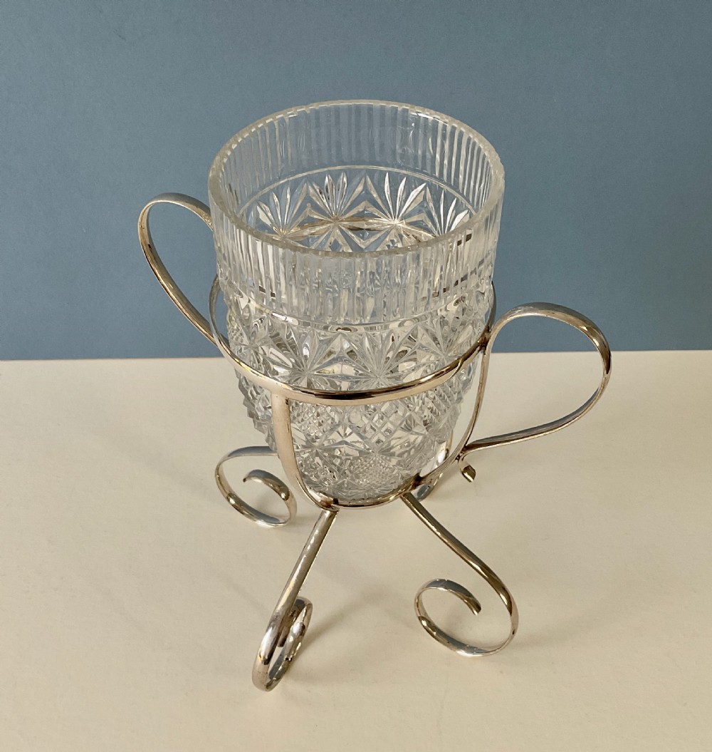A clear cut-glass cylindrical vase featuring diamond motifs resting inside a silver-plated wire frame with scrolled handles and feet. View V