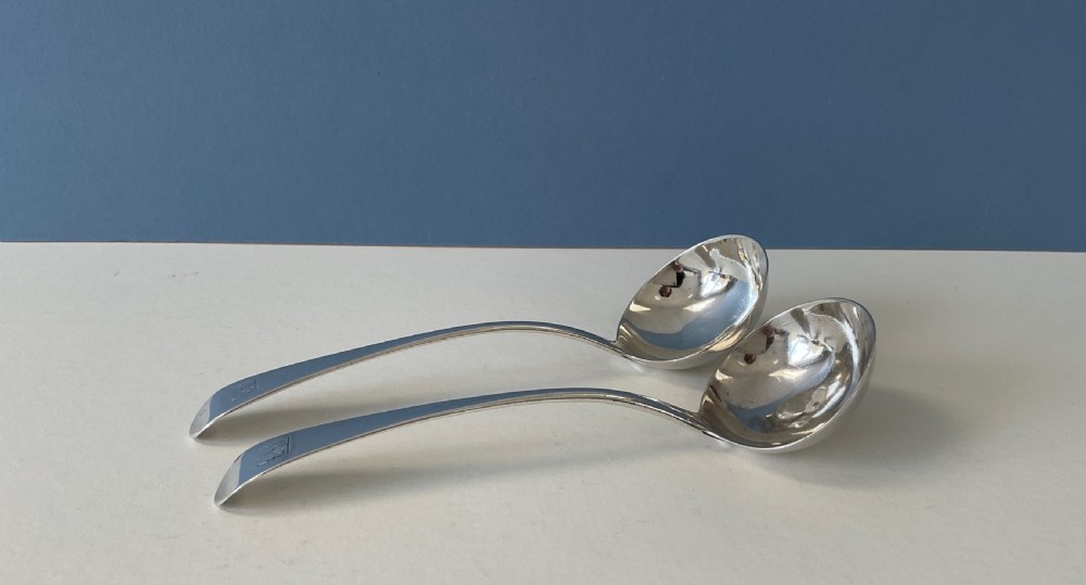 A pair of Georgian sterling silver ladles featuring curved handles with engraved crests and polished round bowls.
