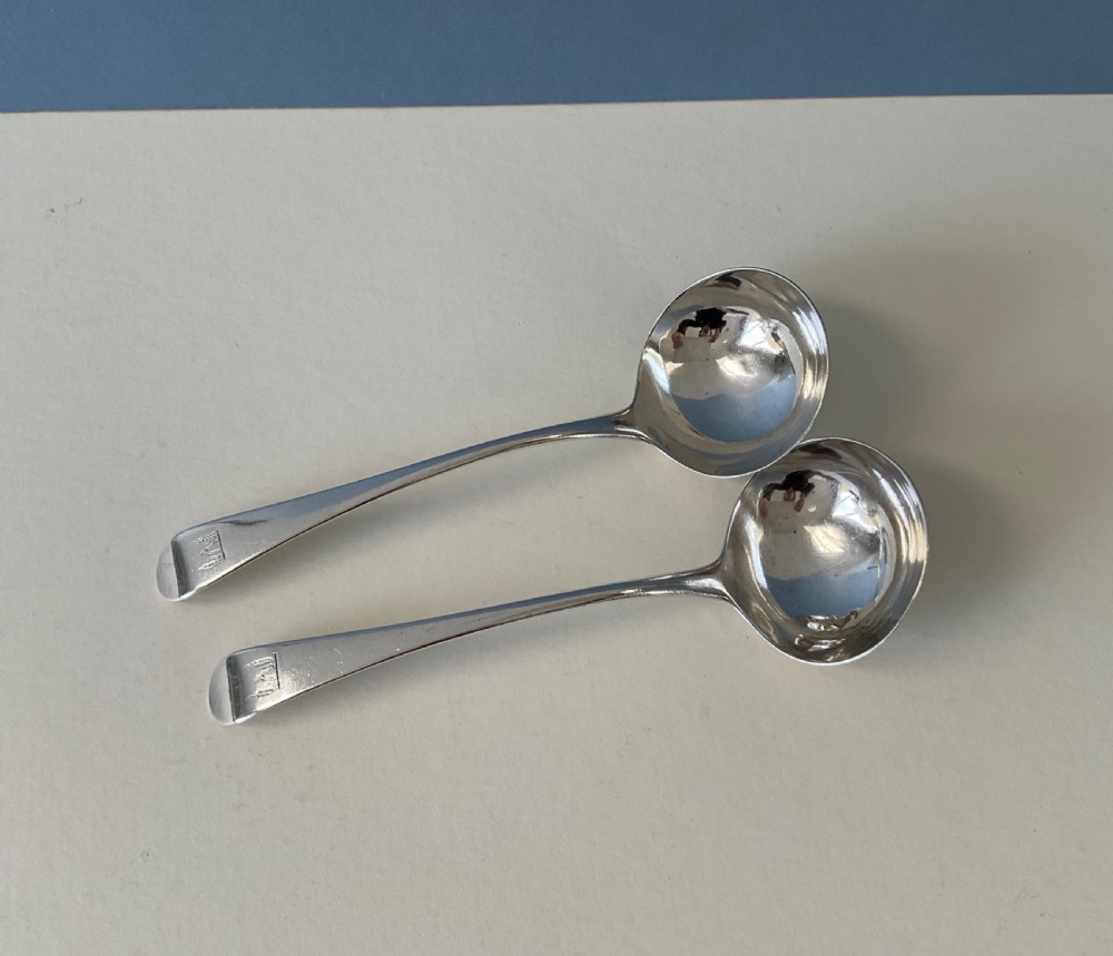 A pair of Georgian sterling silver ladles featuring curved handles with engraved crests and polished round bowls. View II
