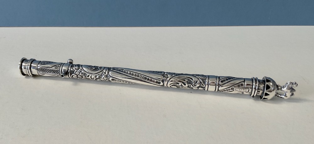 An antique cylindrical silver sealing wax holder decorated with intricate chased scrollwork, floral motifs, and a sculpted animal finial.