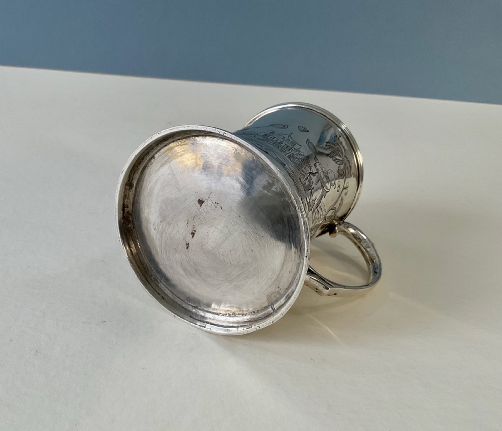 A silver mug featuring detailed Chinoiserie engravings of figures playing battledore and shuttlecock alongside a pagoda, fitted with a loop handle and a gold interior. View II