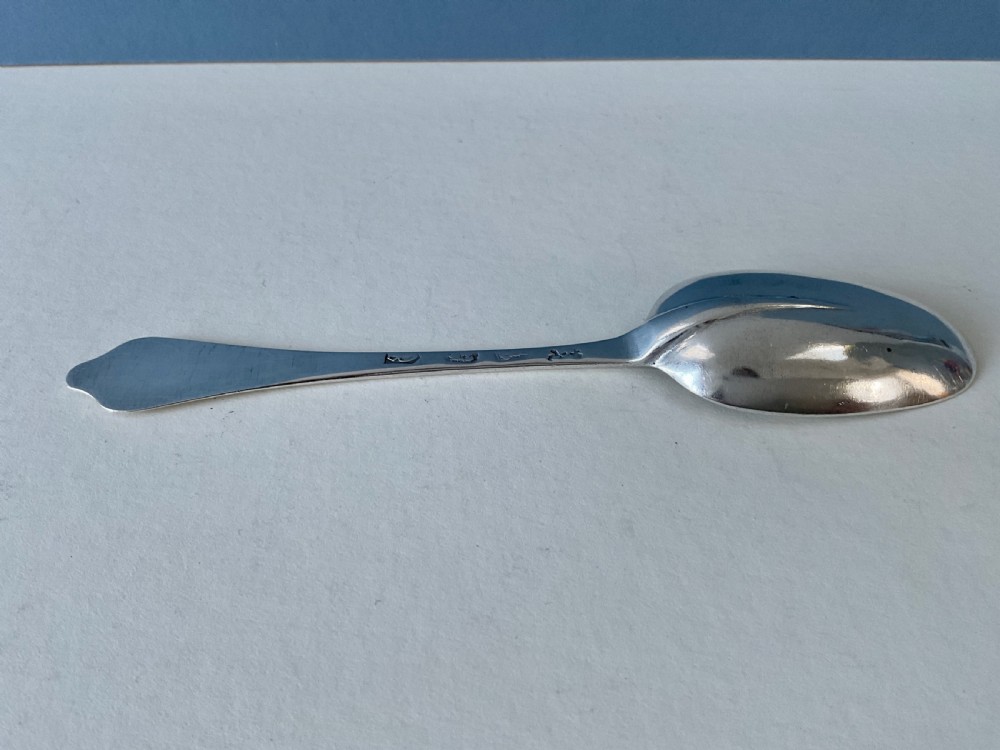 An antique silver spoon featuring an oval bowl and a flat stem with a shaped terminal. View VII