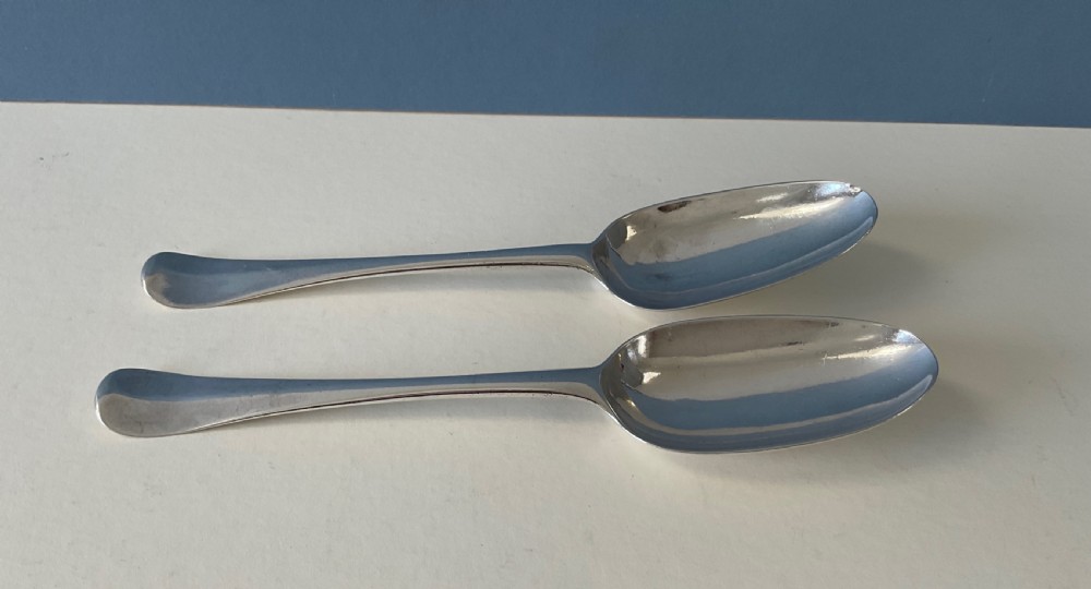 A pair of George I sterling silver spoons featuring elongated oval bowls and smooth Hanoverian stems with upturned terminals.