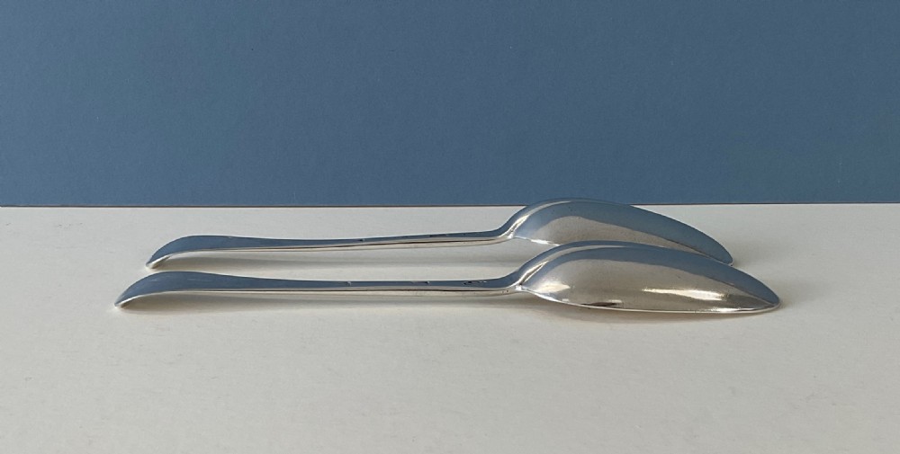 A pair of George I sterling silver spoons featuring elongated oval bowls and smooth Hanoverian stems with upturned terminals. View V