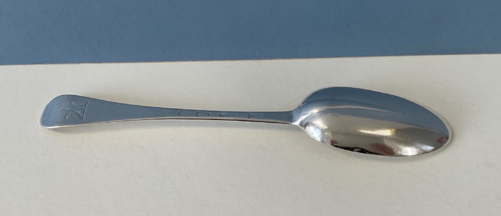 A single George I sterling silver spoon with a central ridge handle, upturned terminal, and an oval bowl against a split blue and white background. View III