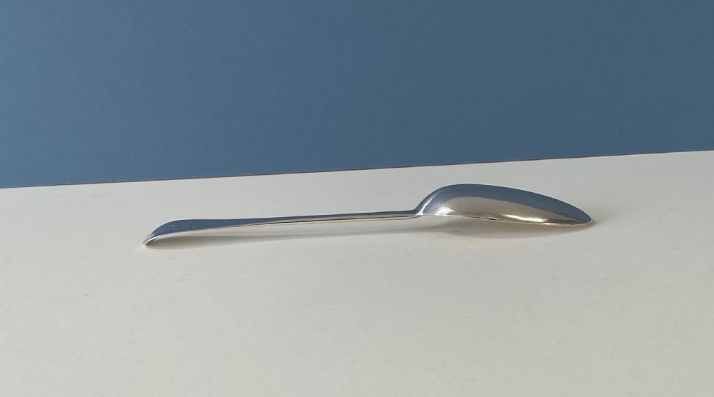 A single George I sterling silver spoon with a central ridge handle, upturned terminal, and an oval bowl against a split blue and white background. View IV