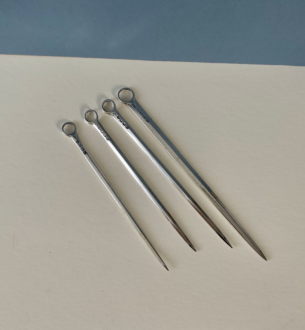A set of four graduating solid silver skewers featuring simple ring terminals and stamped British hallmarks along the upper blades.