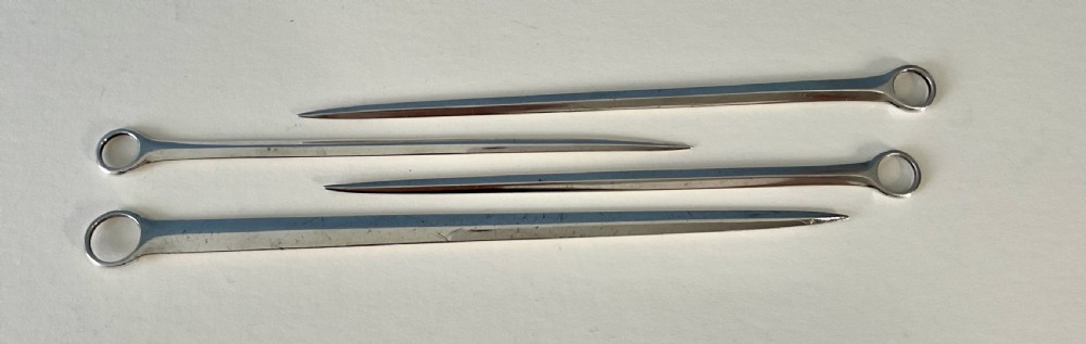 A set of four graduating solid silver skewers featuring simple ring terminals and stamped British hallmarks along the upper blades. View III