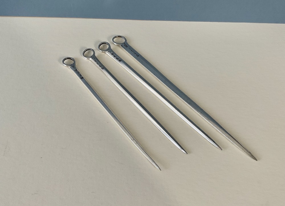 A set of four graduating solid silver skewers featuring simple ring terminals and stamped British hallmarks along the upper blades. View IV