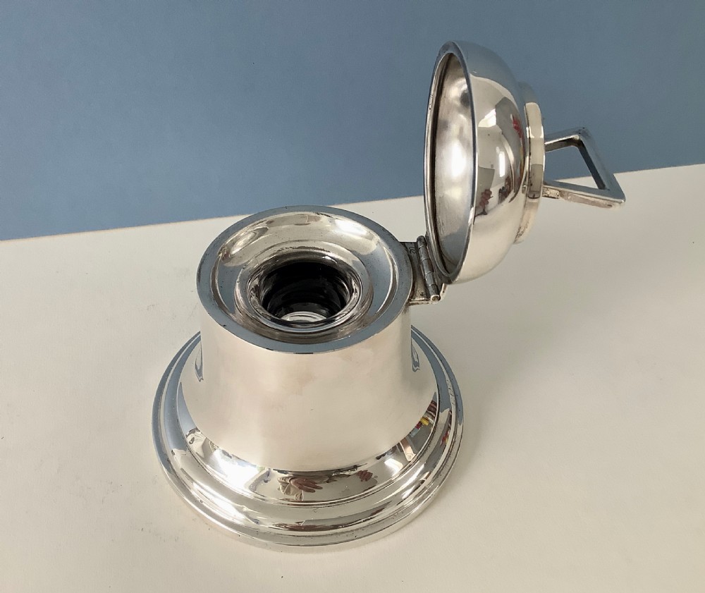 A polished silver Art Deco inkwell shaped like a bell with a geometric triangular handle on the lid. View II