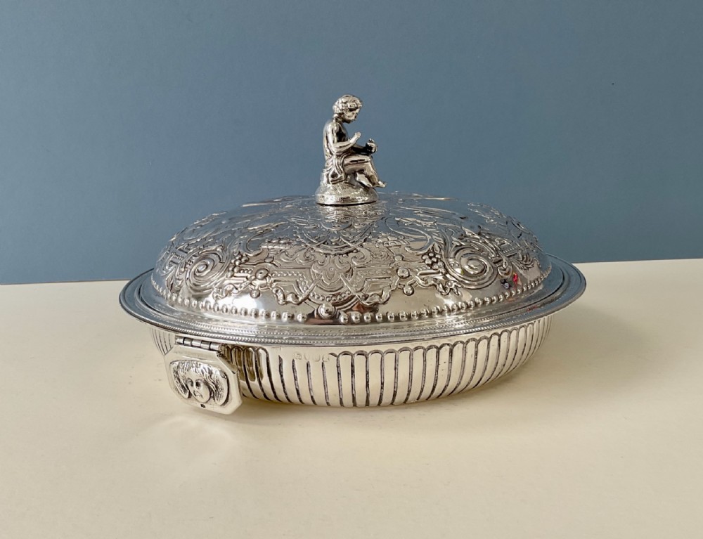An ornate round Georgian solid silver entree dish featuring a domed lid decorated with repousse scrolling motifs, a figural finial, and a beaded rim. View IV