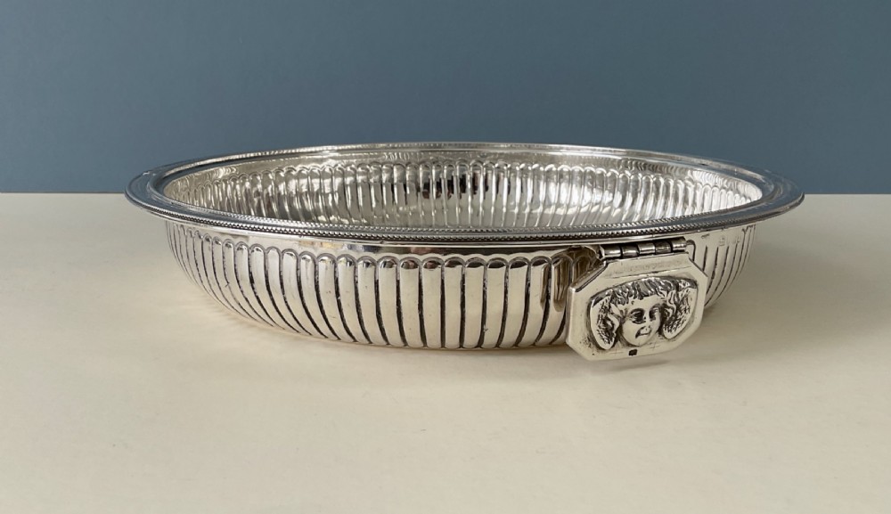 An ornate round Georgian solid silver entree dish featuring a domed lid decorated with repousse scrolling motifs, a figural finial, and a beaded rim. View VII
