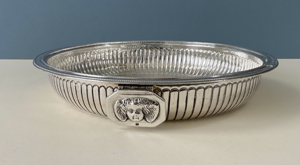 An ornate round Georgian solid silver entree dish featuring a domed lid decorated with repousse scrolling motifs, a figural finial, and a beaded rim. View IX