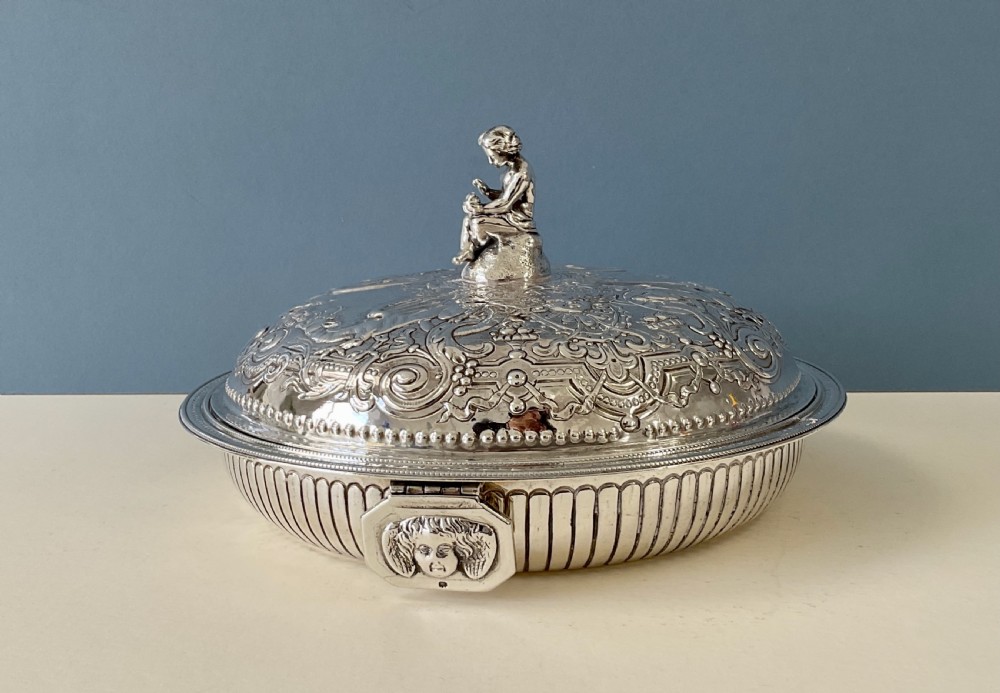 An ornate round Georgian solid silver entree dish featuring a domed lid decorated with repousse scrolling motifs, a figural finial, and a beaded rim. View XI