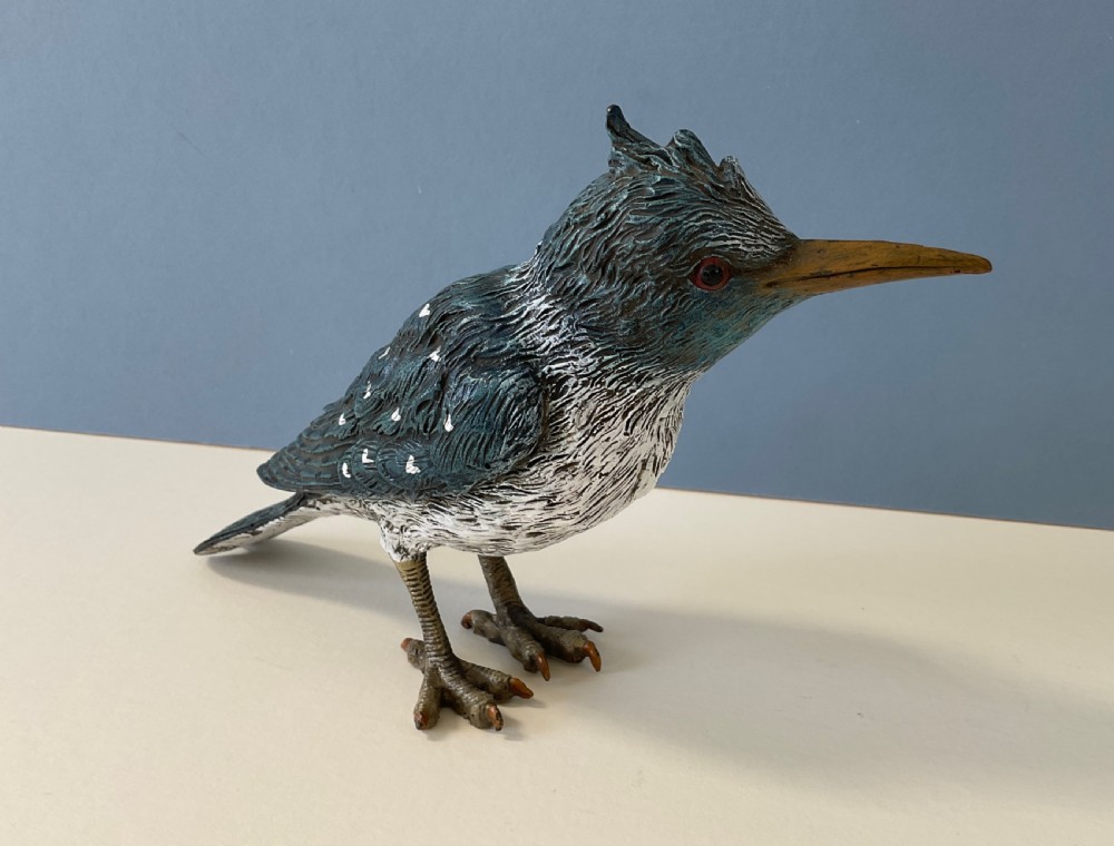 An antique cold-painted bronze figure of a crested kingfisher bird with blue, white, and bronze details standing on two legs.
