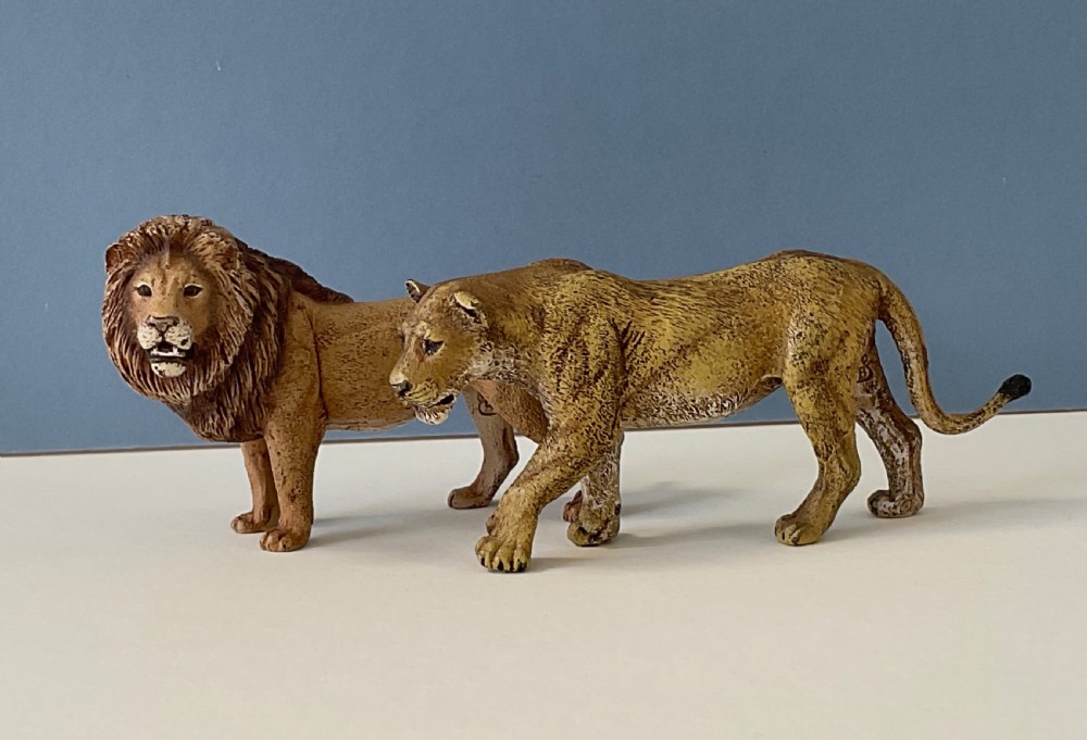 A pair of cold-painted bronze statuettes depicting a male lion and a lioness in realistic tawny brown tones.