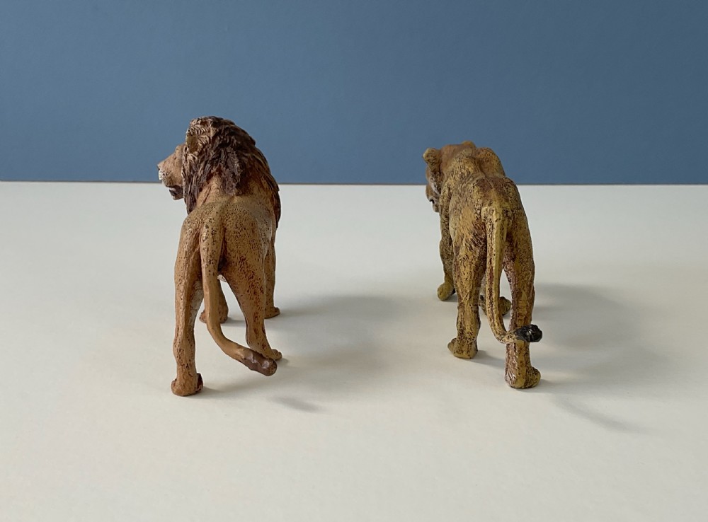 A pair of cold-painted bronze statuettes depicting a male lion and a lioness in realistic tawny brown tones. View IV