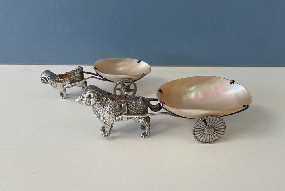 A pair of antique silver novelty pin cushions featuring detailed dog figures pulling mother-of-pearl shell carts on two wheels. View V