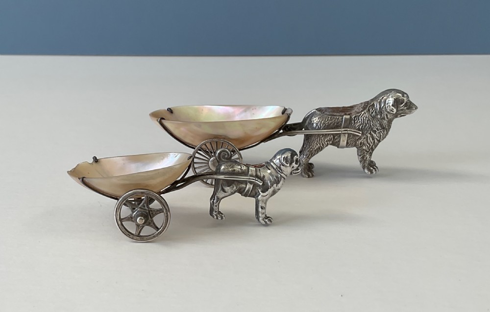 A pair of antique silver novelty pin cushions featuring detailed dog figures pulling mother-of-pearl shell carts on two wheels. View VI