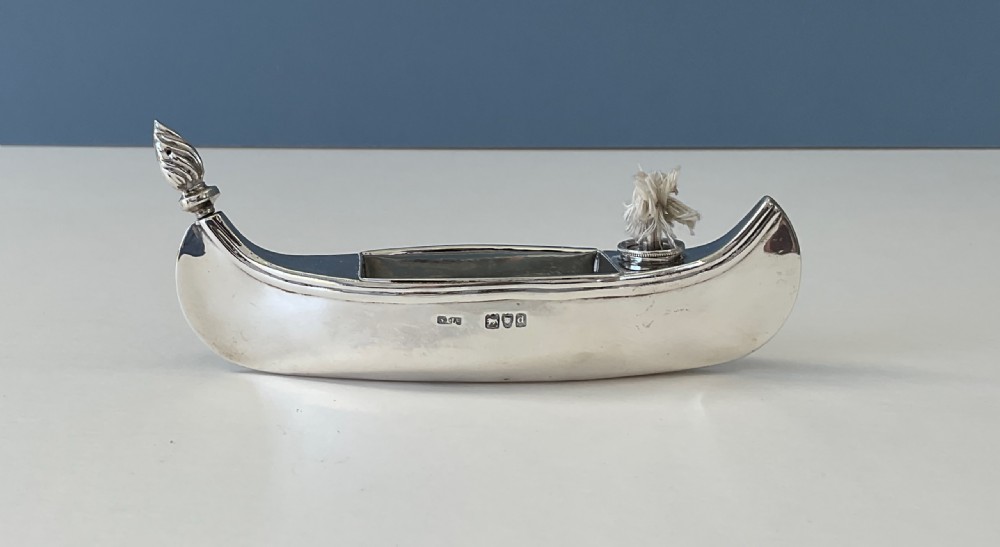 A hallmarked sterling silver table lighter shaped like a canoe with a central wick and a flame-shaped removable stopper.