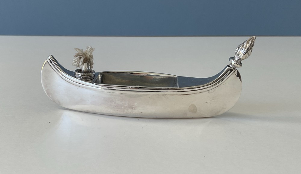 A hallmarked sterling silver table lighter shaped like a canoe with a central wick and a flame-shaped removable stopper. View V