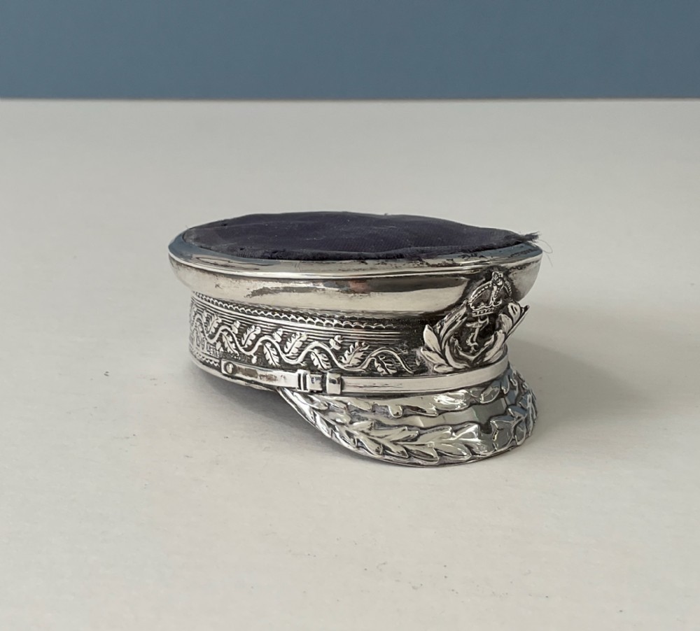 An antique sterling silver novelty pin cushion rendered in the detailed form of a Royal Navy officers cap with a dark fabric top.
