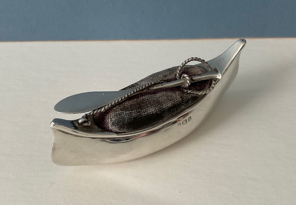 An antique silver canoe-shaped pin cushion featuring a central dark fabric cushion and miniature oar details. View IV