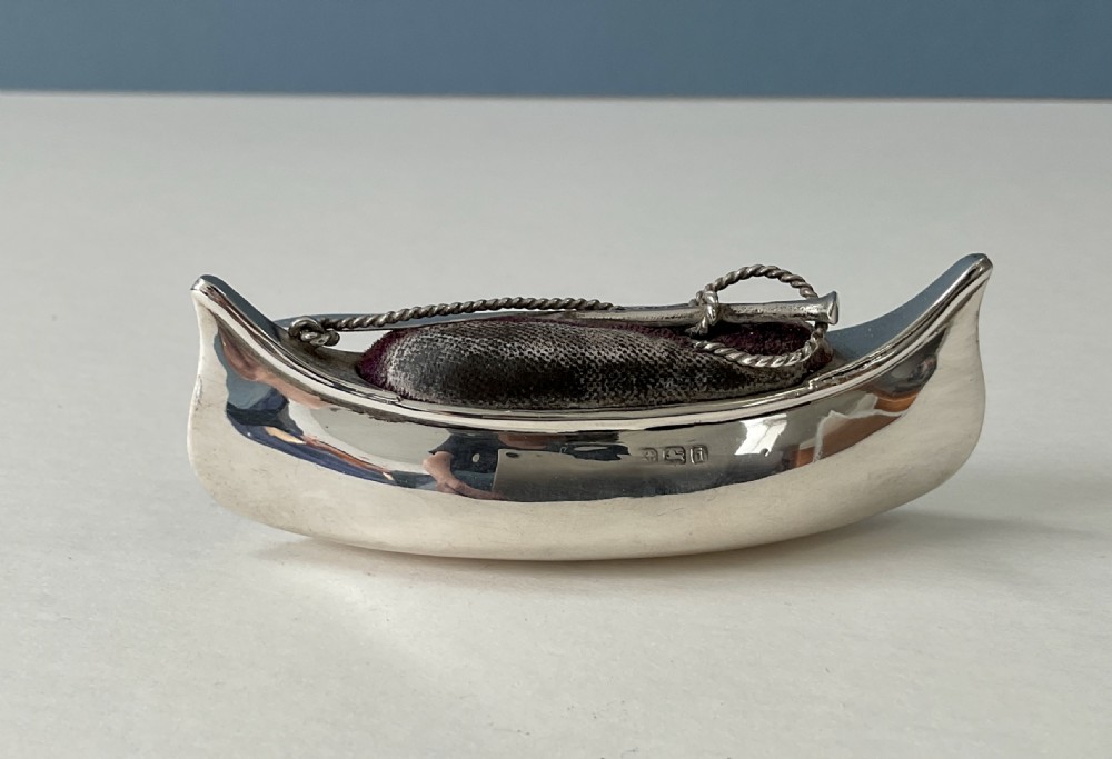 An antique silver canoe-shaped pin cushion featuring a central dark fabric cushion and miniature oar details. View V