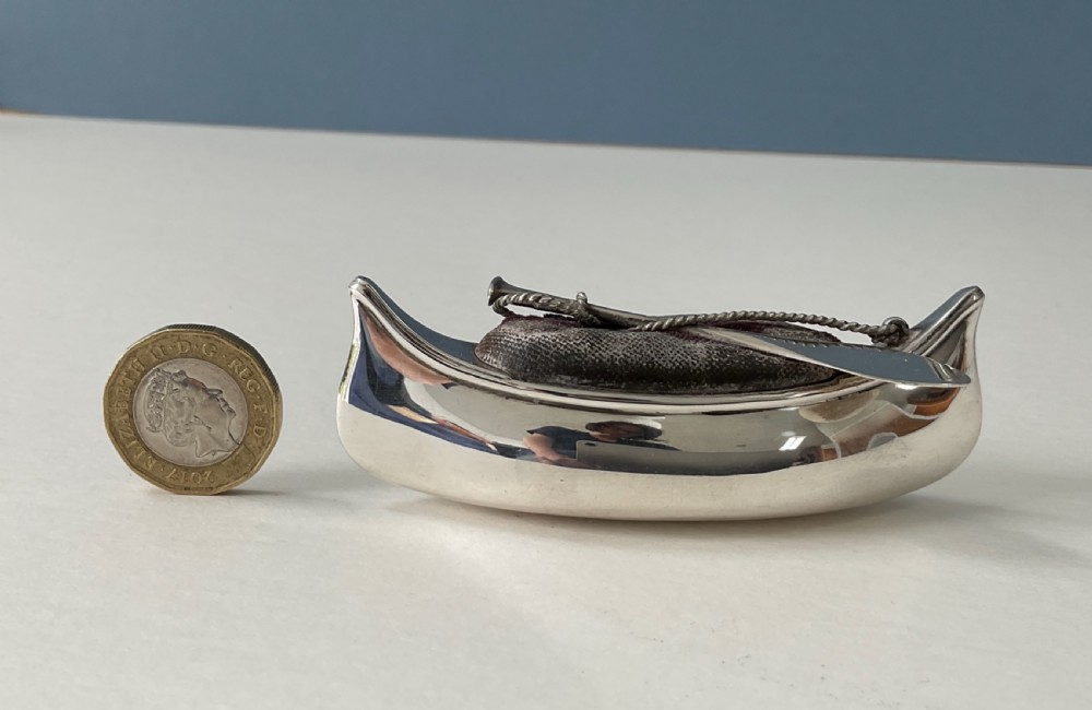 An antique silver canoe-shaped pin cushion featuring a central dark fabric cushion and miniature oar details. View VI