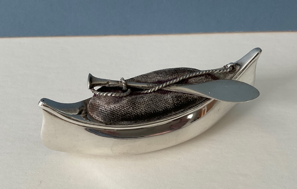 An antique silver canoe-shaped pin cushion featuring a central dark fabric cushion and miniature oar details. View VII