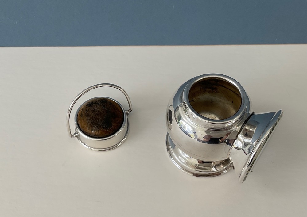 An antique silver novelty pin cushion shaped like a miniature railway lantern with a round convex lens and a dark fabric cushion top. View II