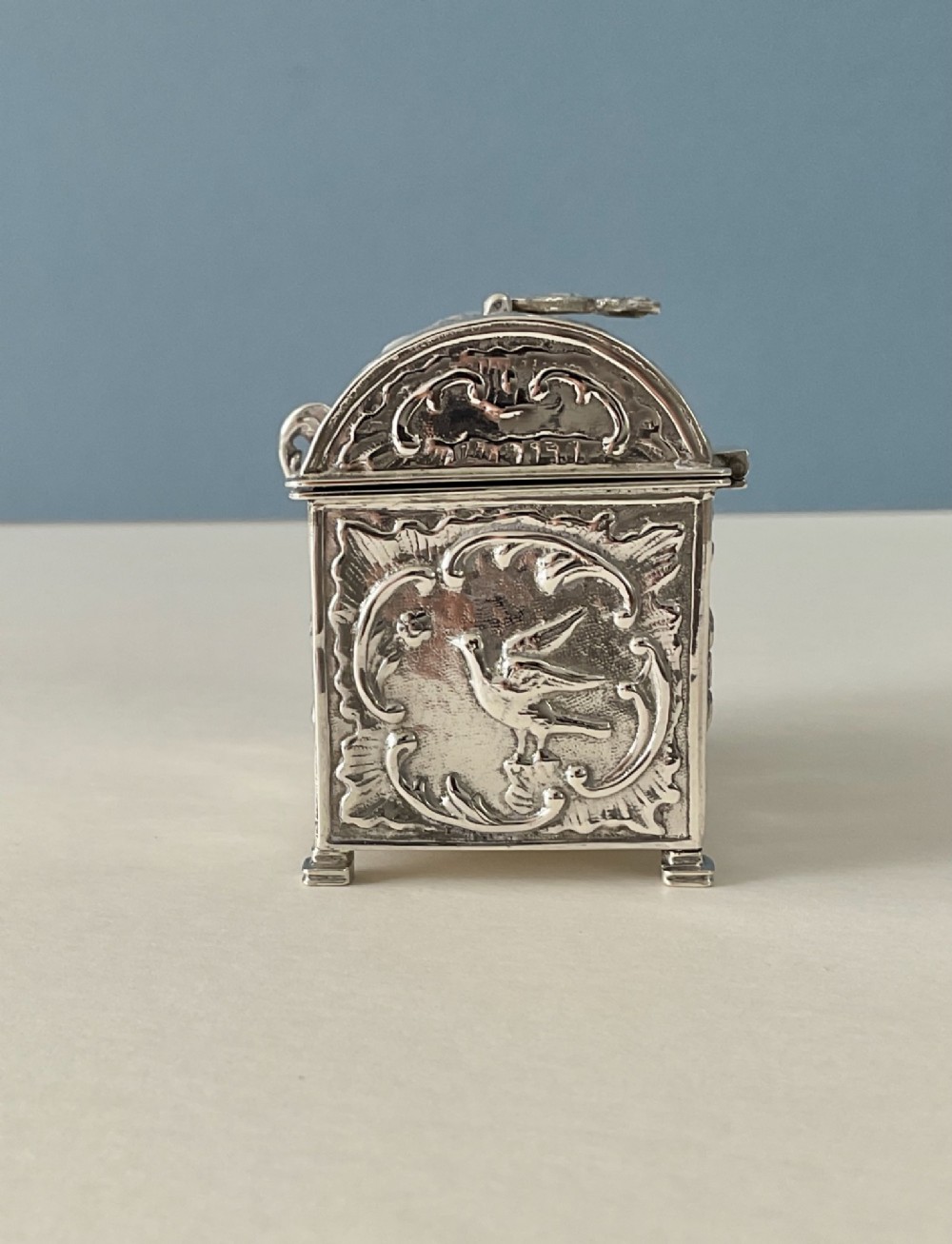 A small rectangular silver marriage casket featuring a domed lid, top handle, bracket feet, and intricate repousse scrollwork depicting birds and floral motifs. View III