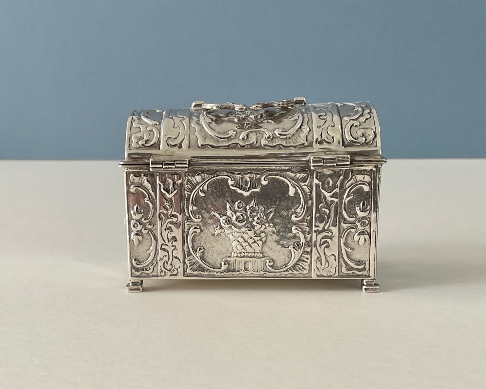 A small rectangular silver marriage casket featuring a domed lid, top handle, bracket feet, and intricate repousse scrollwork depicting birds and floral motifs. View IV