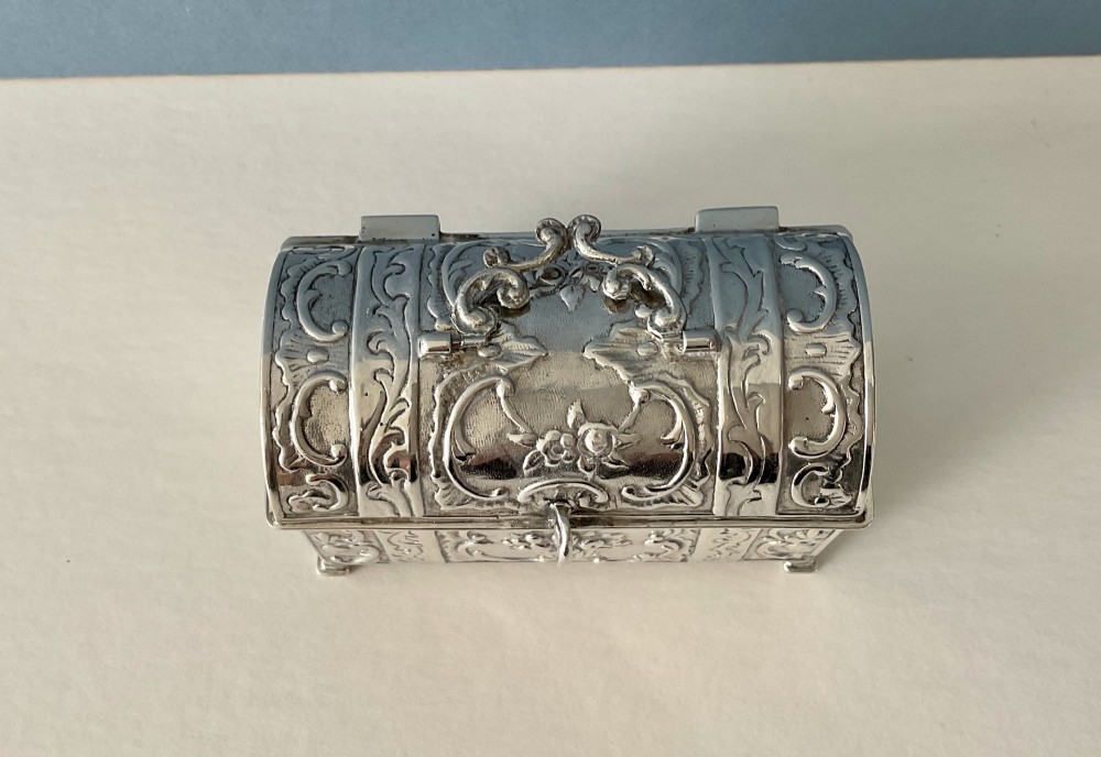 A small rectangular silver marriage casket featuring a domed lid, top handle, bracket feet, and intricate repousse scrollwork depicting birds and floral motifs. View VI