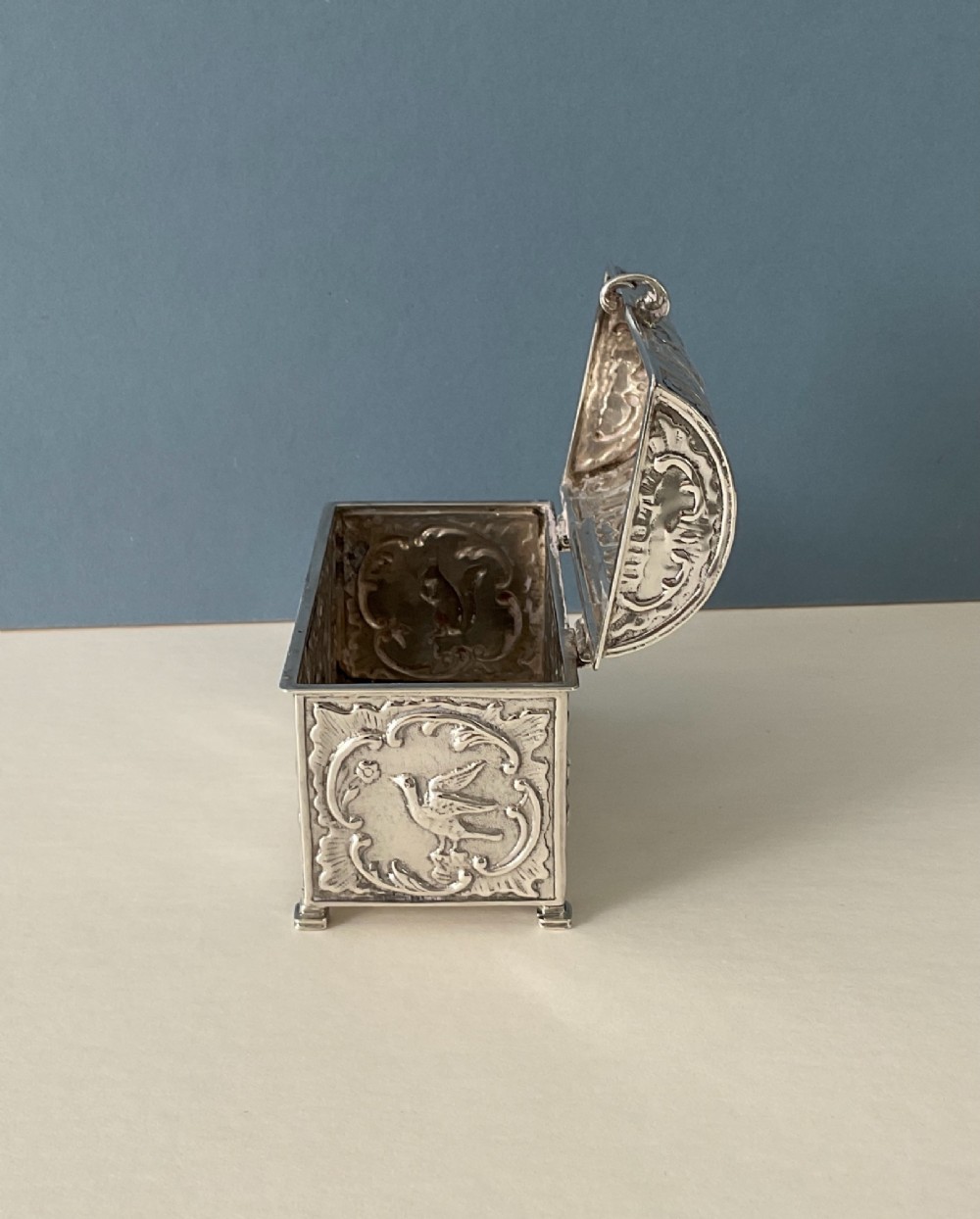 A small rectangular silver marriage casket featuring a domed lid, top handle, bracket feet, and intricate repousse scrollwork depicting birds and floral motifs. View VIII