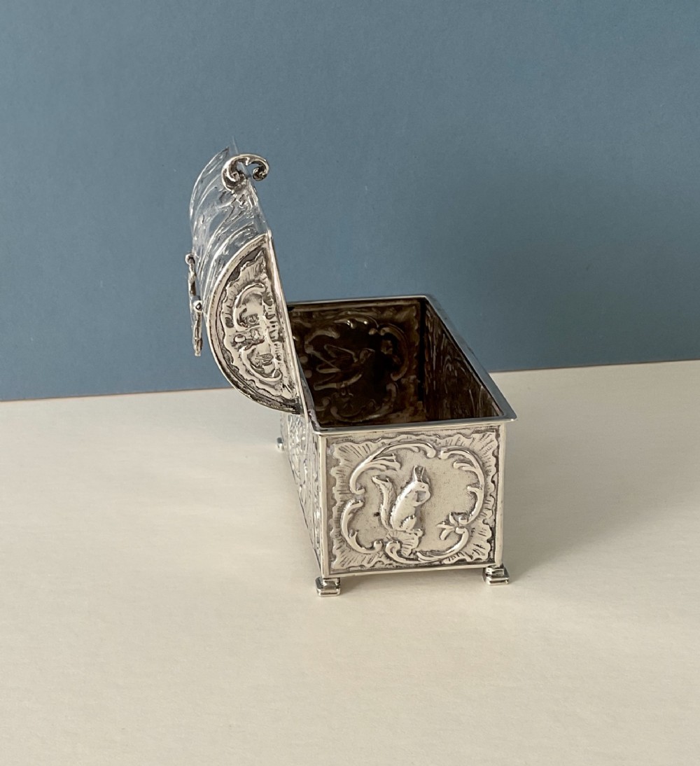 A small rectangular silver marriage casket featuring a domed lid, top handle, bracket feet, and intricate repousse scrollwork depicting birds and floral motifs. View IX
