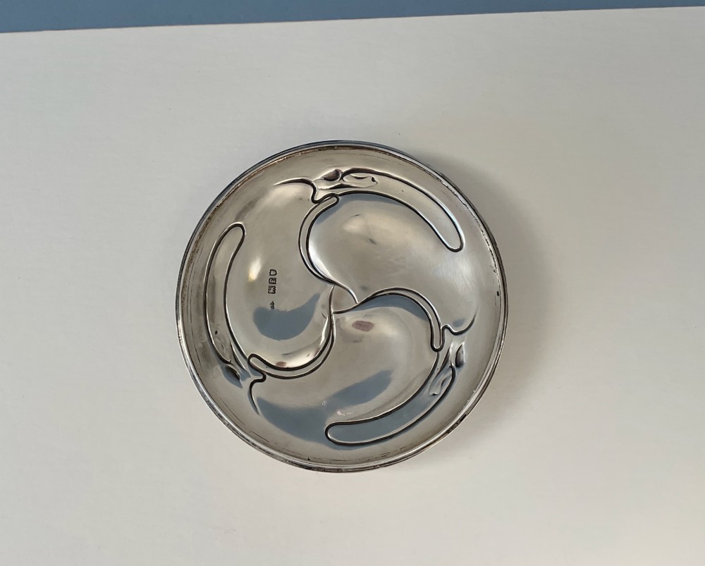 An Art Nouveau silver lidded bowl featuring high looping handles and an elongated pedestal stem against a plain blue background. View VI