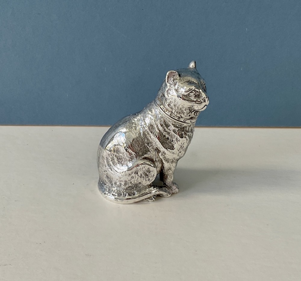 A small silver pepper caster crafted in the form of a seated cat with detailed chased fur and a collar.