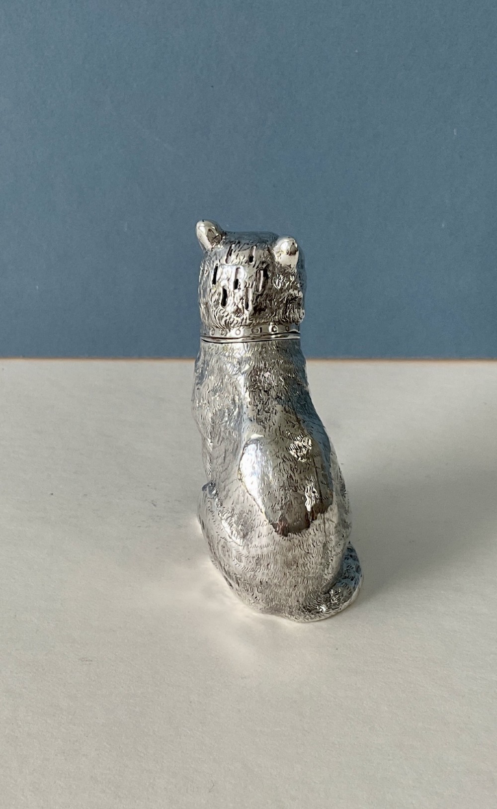 A small silver pepper caster crafted in the form of a seated cat with detailed chased fur and a collar. View II