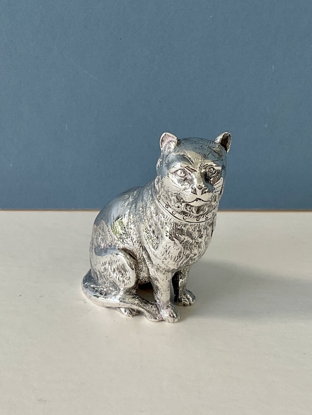A small silver pepper caster crafted in the form of a seated cat with detailed chased fur and a collar. View IX