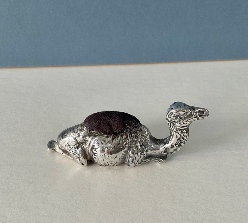 An antique silver novelty pin cushion cast in the form of a seated camel with a dark fabric cushion integrated into its back. View V