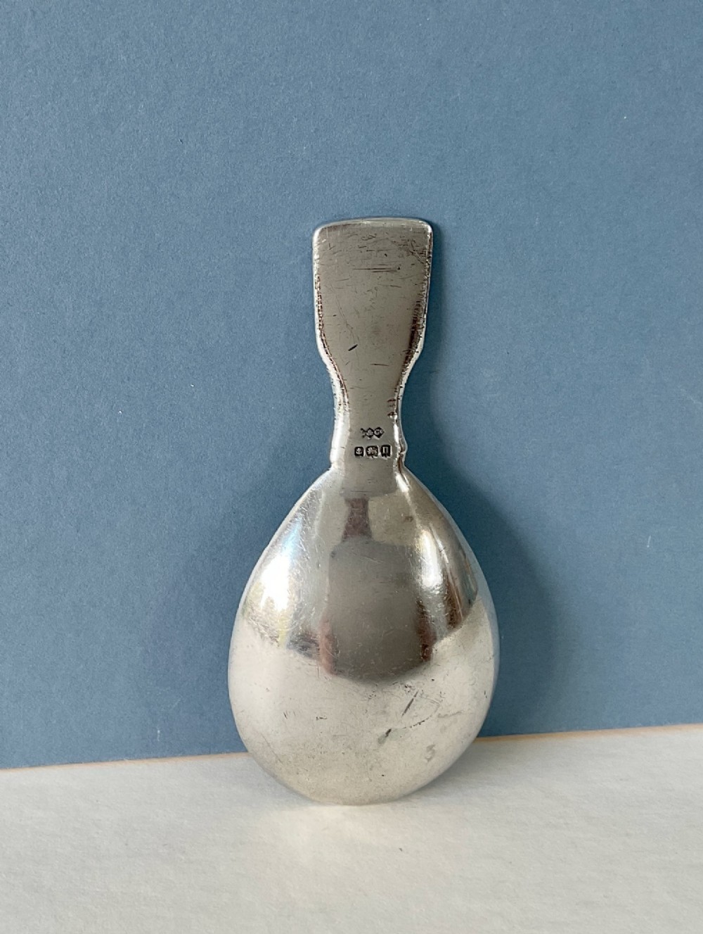 An antique sterling silver caddy spoon featuring a teardrop bowl and flat handle decorated with geometric basketweave engraving. View II