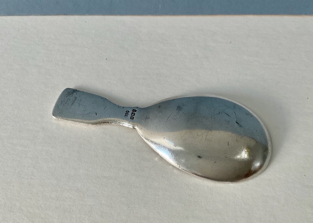 An antique sterling silver caddy spoon featuring a teardrop bowl and flat handle decorated with geometric basketweave engraving. View III
