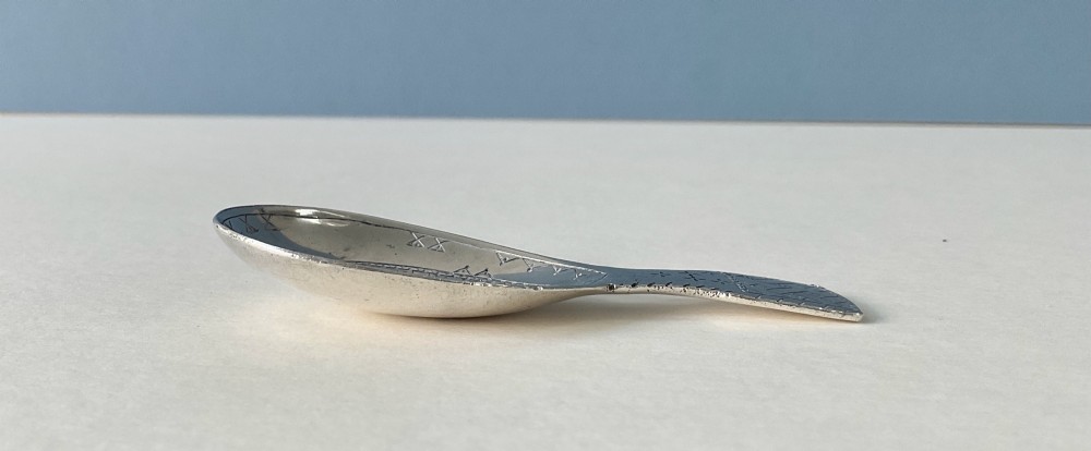 An antique sterling silver caddy spoon featuring a teardrop bowl and flat handle decorated with geometric basketweave engraving. View IV