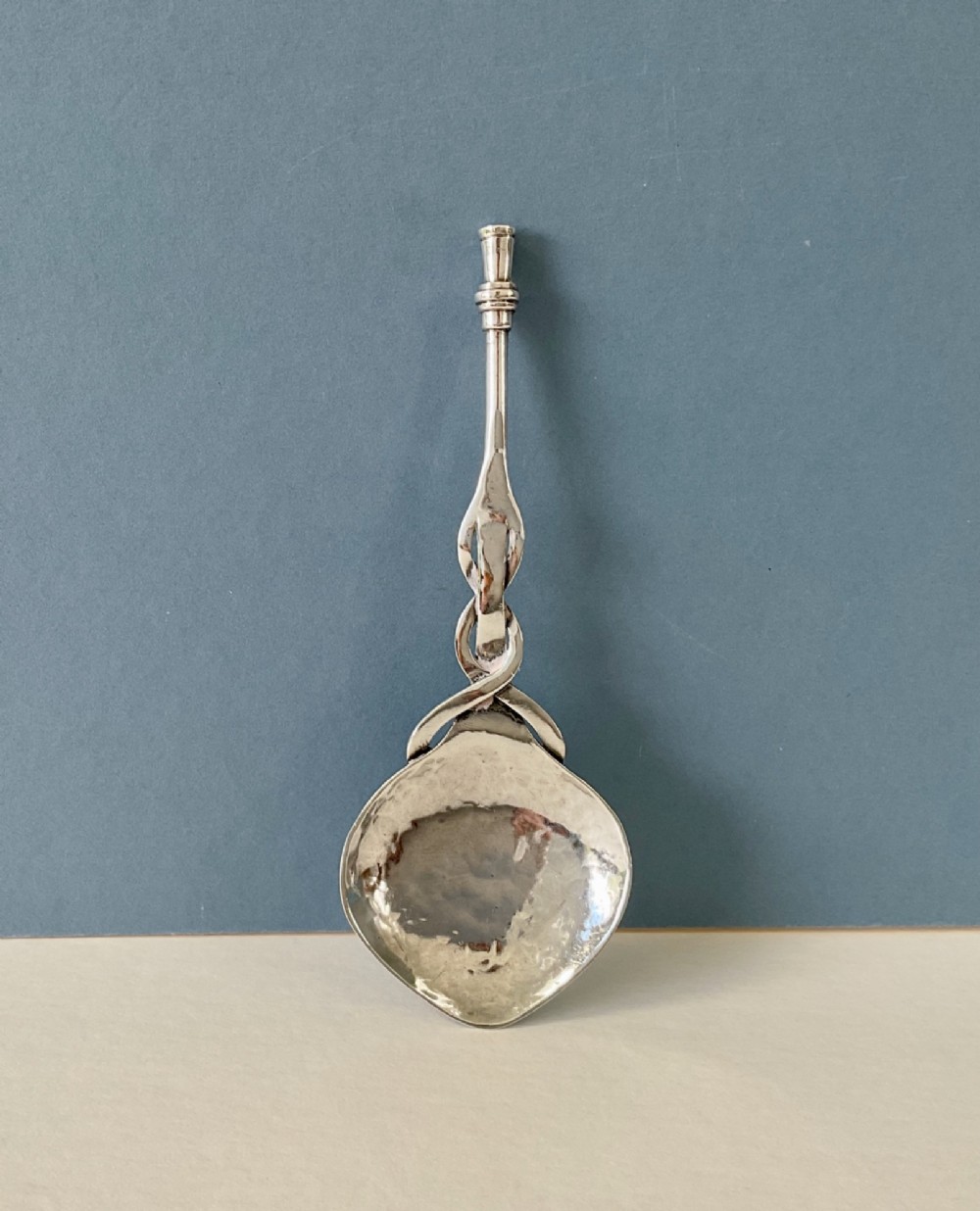 An Arts and Crafts sterling silver caddy spoon featuring a hand-hammered bowl and an intertwined stem handle.