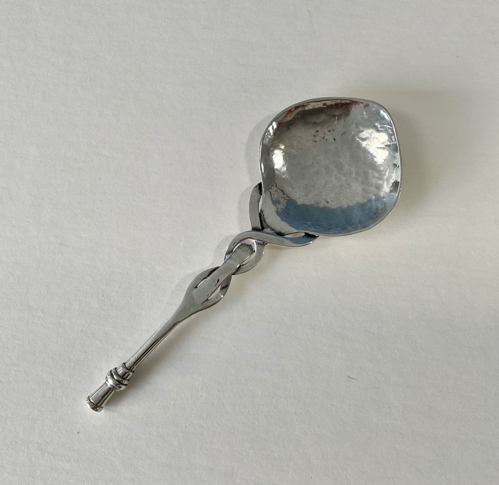 An Arts and Crafts sterling silver caddy spoon featuring a hand-hammered bowl and an intertwined stem handle. View V