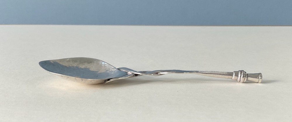 An Arts and Crafts sterling silver caddy spoon featuring a hand-hammered bowl and an intertwined stem handle. View VI