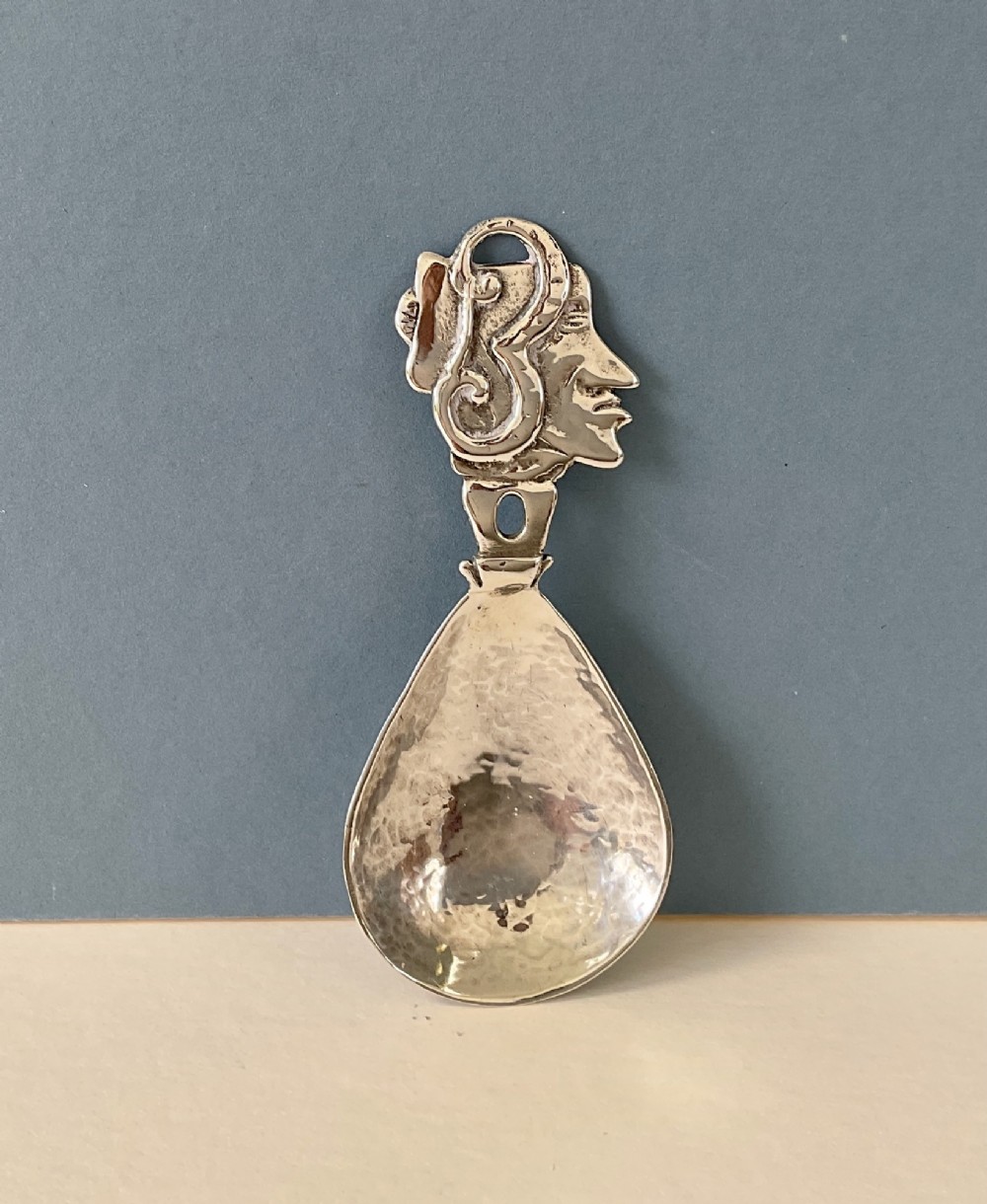 A hand-hammered silver caddy spoon featuring a stylized profile head handle and a teardrop-shaped planished bowl.