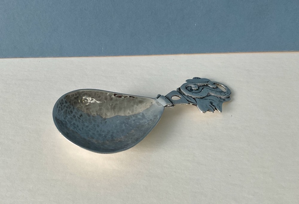 A hand-hammered silver caddy spoon featuring a stylized profile head handle and a teardrop-shaped planished bowl. View V