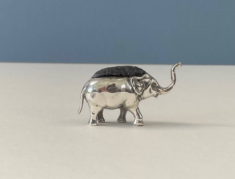 A miniature silver novelty pin cushion cast in the shape of an elephant with a dark fabric insert set into its back.